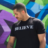 A man wearing the black Believe tee, BELIEVE printed across the chest