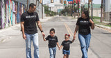 Two adults and two children walking down a San Antonio street, all wearing the black Believe tee